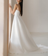 Fototapeta premium Side view of beautiful brunet bride in long white wedding dress with the naked back. Gorgeous sleeveless wedding dress