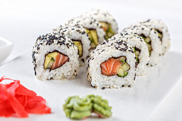 Sushi with salmon on a white plate with wasabi, ginger, soy, chopsticks on a white background