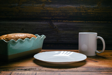 Homemade sponge cake in blue ceramic mold, white cup and white plate on wooden table.