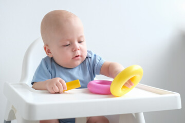 cute baby boy playing with colorful plastic toys at child chair. early children development