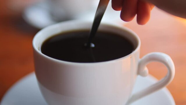 Close up of woman hand stiring black coffee in the cup with a teaspoon.