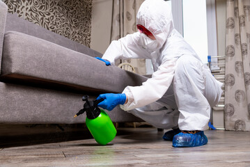 An exterminator in work clothes sprays pesticides with a spray gun. Fight against insects in apartments and houses. Disinsection of the premises