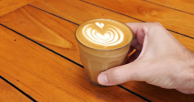 Man take glass of latte with picture on foam from the table, close up slow motion shot. Coffee drink with short-living art on neat foam at top, a popular attraction for cafe customers