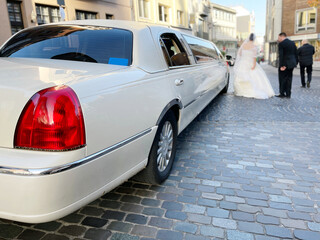 Wedding couple with stretched limousine after wedding ceremony