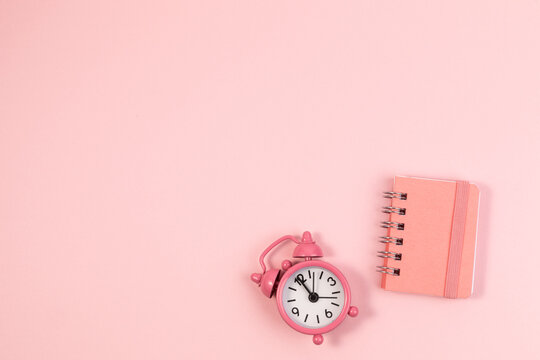 small alarm clock and clean notebook pastel pink background.