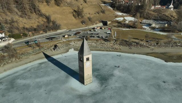 Drone panning shot tourism walking to the sunken church of Graun on a frozen lake in Italy.