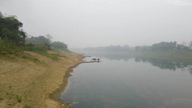 A drone ascending above the riverbank of Surma river to reveal a small fishing boat ties to a pole