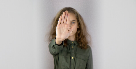 Portrait of a serious blonde teenage girl standing with outstretched hand showing stop gesture...