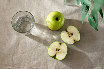Green apples ang glass of water on beige table, minimalist spring summer composition, copy space