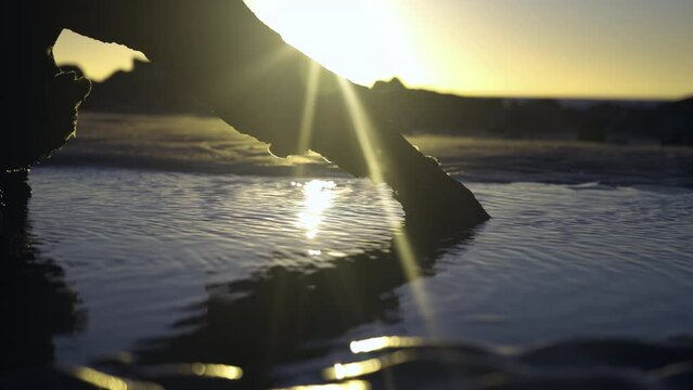 Tight static shot of Sunrise with driftwood and puddle on the beach