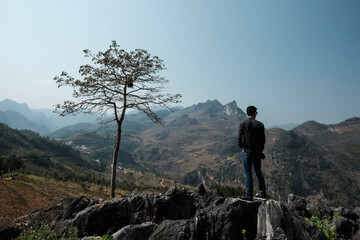 Rear view of man standing on rocks against mountains and clear sky