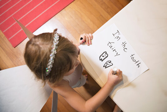 High angle view of girl wearing tooth fairy costume while writing on paper at home