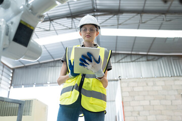 Female engineer control robot arm by computer tablet in workshop. Woman technician working with...