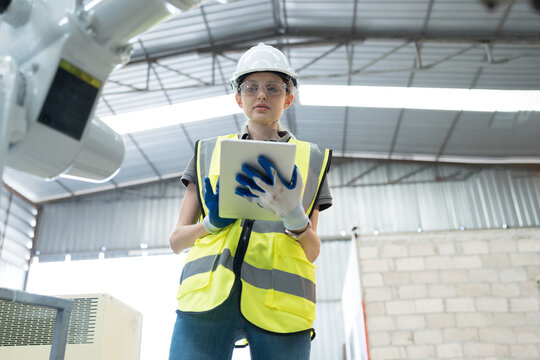 Female engineer control robot arm by computer tablet in workshop. Woman technician working with control automatic robot arm system welding. Industry robot manufacturing technology
