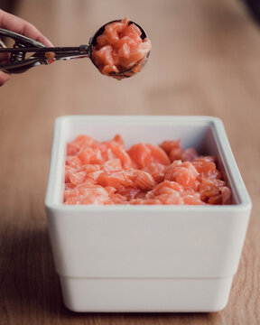 Cropped Hand Of Person Holding Chopped Salmons With Serving Scoop Over Bowl