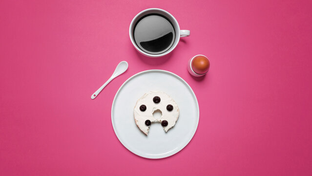 Overhead view of bun with egg and coffee on pink background