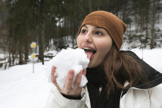 Young woman looking away while licking snow in forest during winter