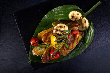 Overhead view of grilled halloumi cheese with cherry tomatoes, peppers and zucchini served in leaf on table