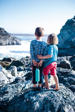 Rear view of siblings looking at sea while standing on rocks during sunny day