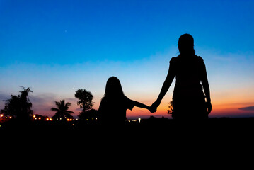 Rear view of silhouette mother and daughter holding hands while standing against dramatic sky during sunset