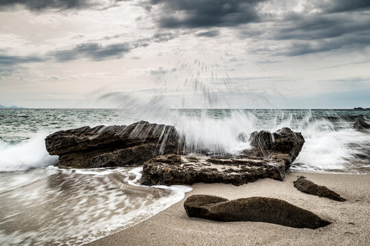 Waves splashing on rocks at beach against cloudy sky