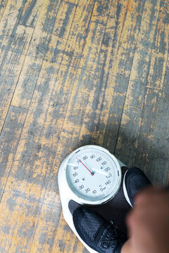 Low section of man checking weight on bathroom scale in gym
