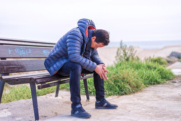 Man sittingo on bench outdoors with head down  on the beach