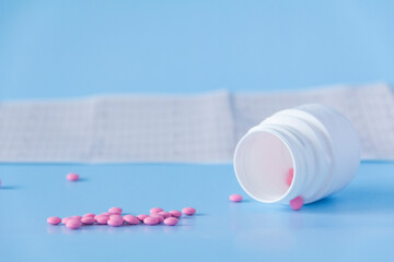 A large handful of pink pills poured out of a white jar on an electrocardiogram of the heart, on a...