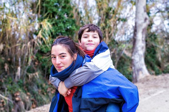 oung boy piggyback on his sister looking at camera and smiling in nature