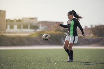 Young female soccer player kicking ball in a stadium.
