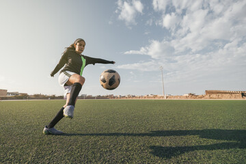 Young female soccer player kicking ball in a stadium