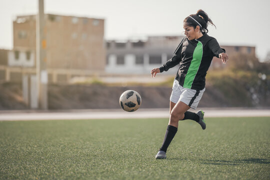 Young female soccer player kicking ball in a stadium. - Powered by Adobe