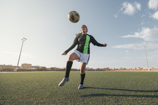 Young female soccer player kicking ball in a stadium.