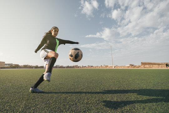 Young female soccer player kicking ball in a stadium