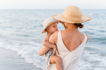 Woman in a straw hat holding a little girl in her arms near the sea