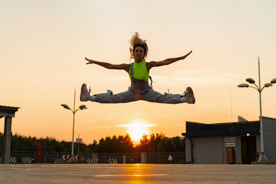 Woman in a split jump against the background of a sunset. - Powered by Adobe