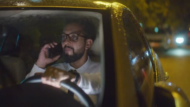 Businessman talking on mobile phone and holding steering wheel while sitting in car at rainy night