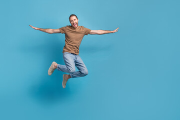 Obraz premium Full length photo of pretty impressed guy dressed beige t-shirt jumping high arms sides empty space isolated blue color background