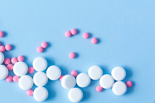 A large handful of white, round pills and pink medicines against a blue background. The concept of a healthy lifestyle and timely medical examination.