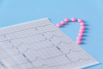 Half of a heart made of pink drugs and an electrocardiogram of the heart, on a blue background. The concept of a healthy lifestyle and timely medical examination.