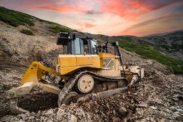 Yellow excavator on new construction site, with the bright sun and nice red sky in the background