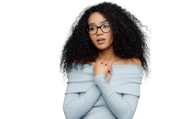 Worried nervous female keeps hands pressed together over chest, has thoughtful expression, wears glasses and long sleeved sweater, focused into distance, isolated on blue background with empty space