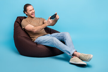 Full length photo of excited funny guy dressed t-shirt bean bag playing game modern device empty...