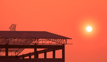 Silhouette of Industrial Building Structure with metal roof outline in under Construction against colorful orange sunset sky background