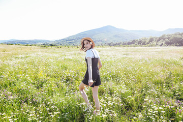 a woman in a straw hat walks in a field with daisies flowers in nature