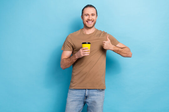 Photo of cool confident guy dressed beige t-shirt showing thumb up enjoying coffee isolated blue color background