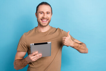 Photo of stylish positive man tail hairdo dressed beige t-shirt hold tablet showing thumb up approve isolated on blue color background