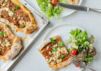 Turkish pide or flatbread with minced meat, feta cheese topping on white kitchen table with plate...