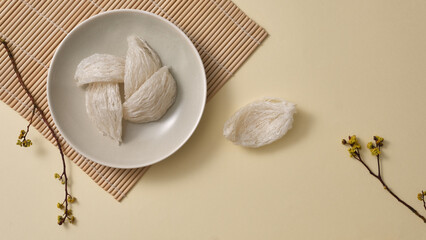Top view of raw bird's nest neatly arranged in round dishes, small flower branches on beige background. Bird's nest is an expensive culinary ingredient for health - Healthy food.
