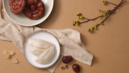 Salanganes nest raw on round dishes, red reishi mushroom, jujube on brown background. There are ingredients for distilling premium bird's nest. Top view, flat lay.